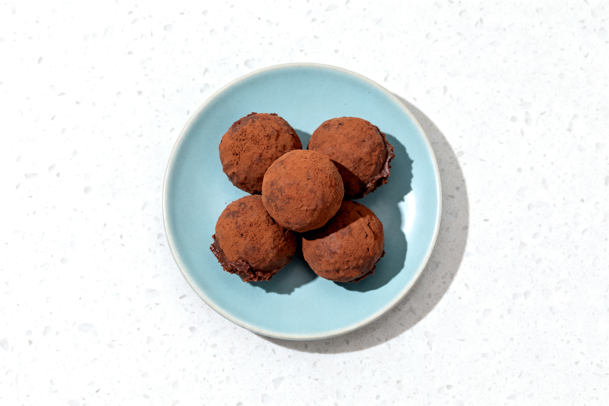 shot of five chocolate cheesecake protein balls arranged in a casual cluster on a light blue cerami