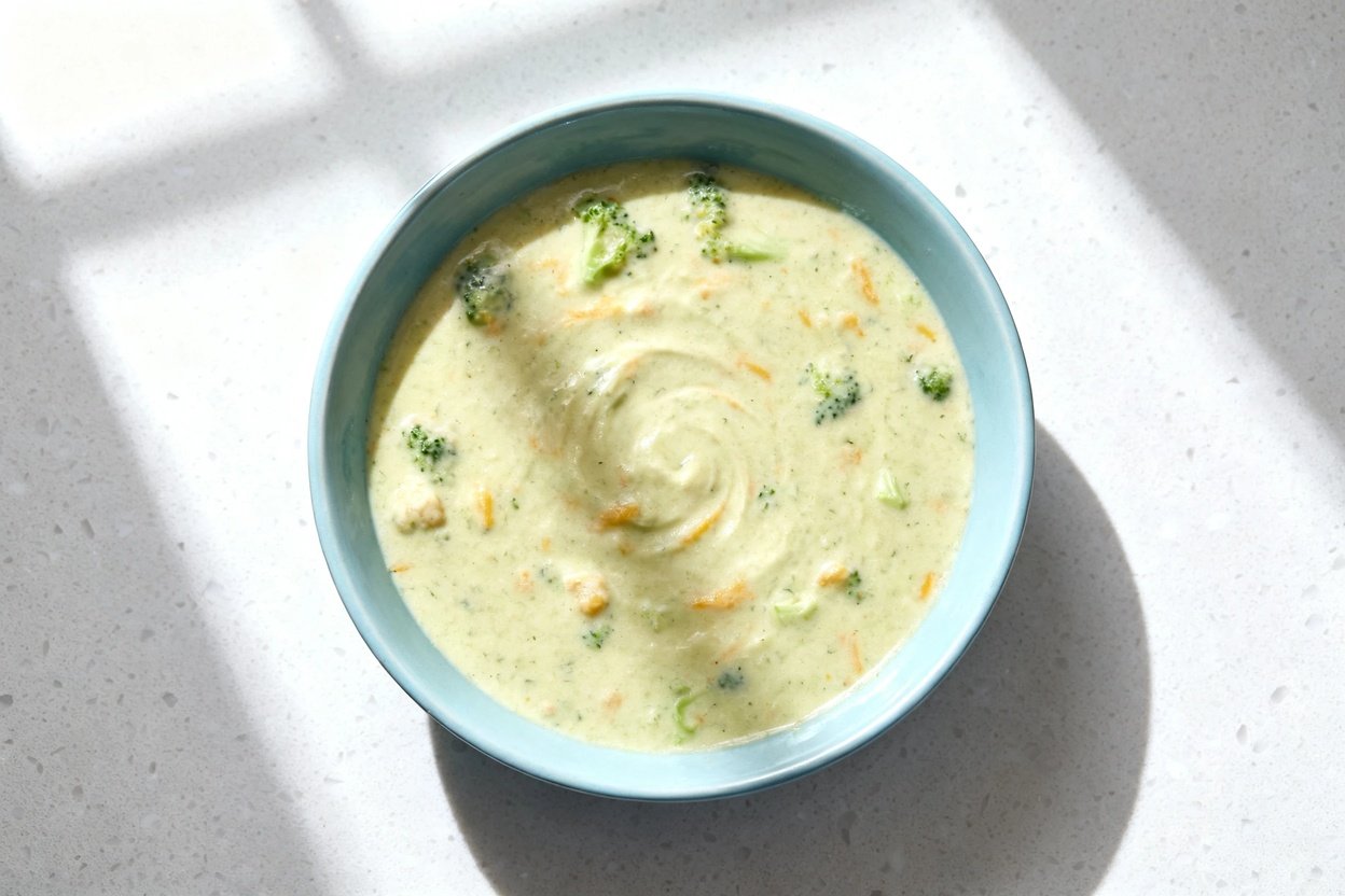 top-down food photo of a single serving of keto creamy broccoli cheddar soup in a light blue ceramic