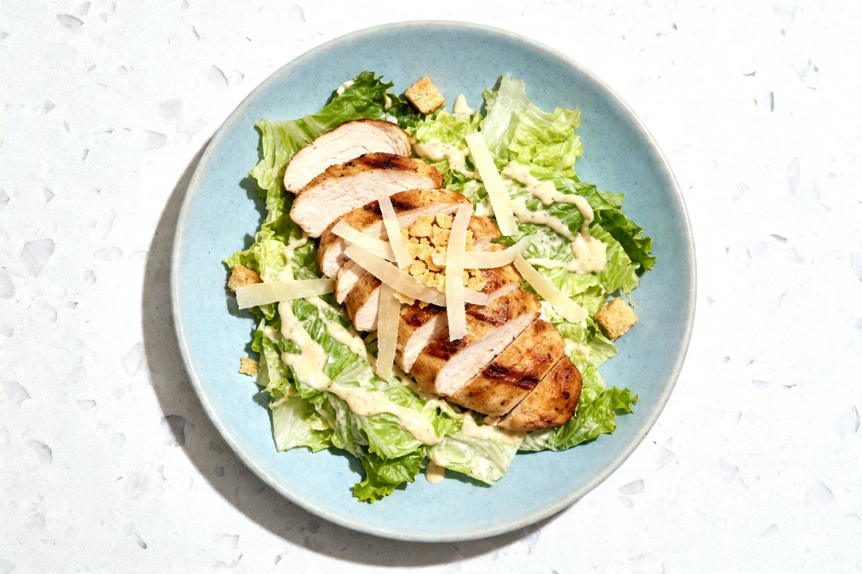 top-down food photograph of a single serving Grilled Chicken Keto Caesar Salad on an identical light