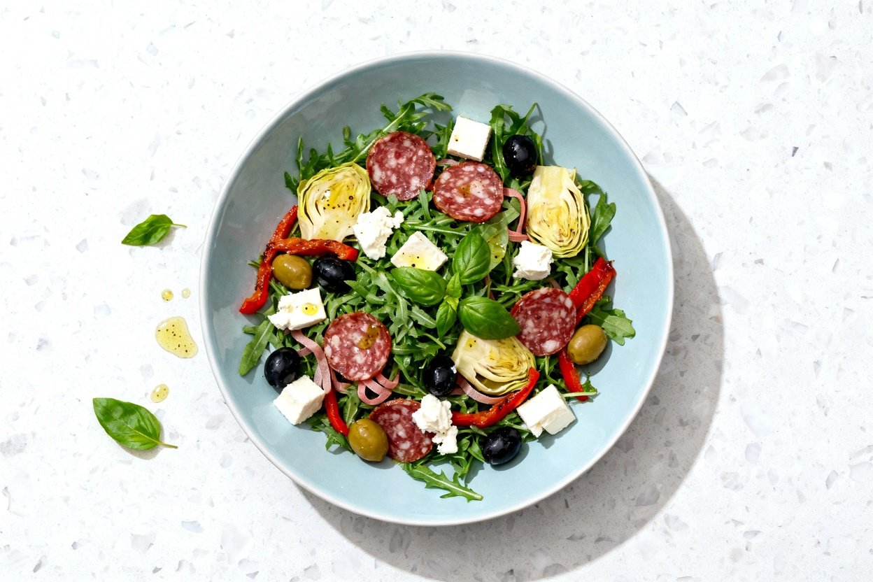 top-down food photo of a single-serving Keto Low Carb Italian Antipasto Salad plated on a light blu