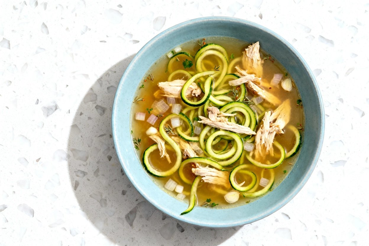 top-down food photo of a single serving of keto chicken zoodle soup centered in a light blue ceramic