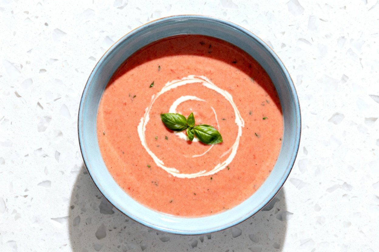top-down food photo of a single serving of creamy keto tomato basil soup: a velvety, pale-red to dee