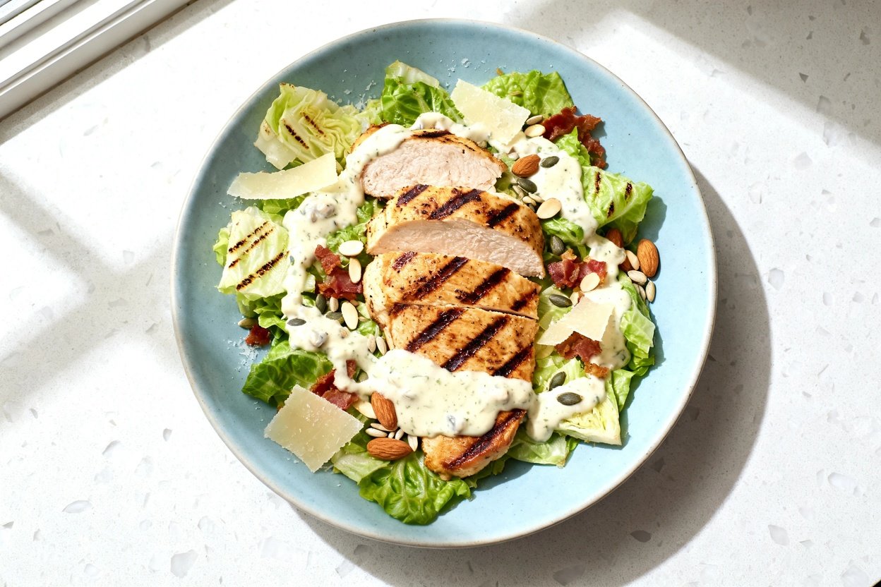 top-down food photo of a single serving grilled keto chicken Caesar salad on an identical light blue