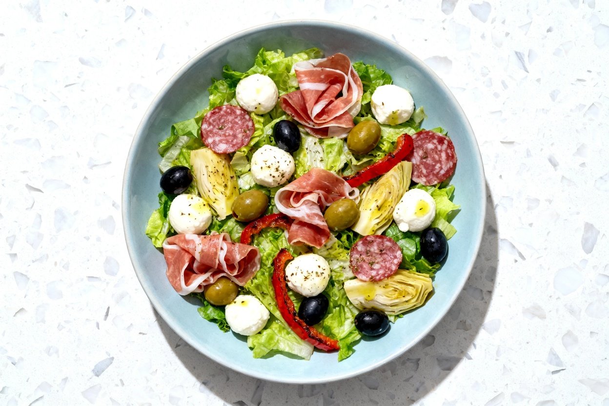 top-down food photograph of a Keto Antipasto Salad Bowl, single serving centered on an identical lig
