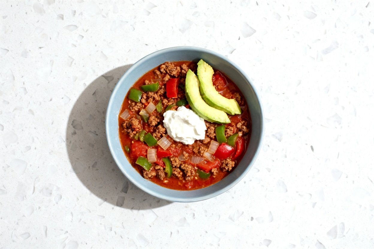 top-down food photo of a single serving of hearty keto beef chili (beanless) centered in a light bl