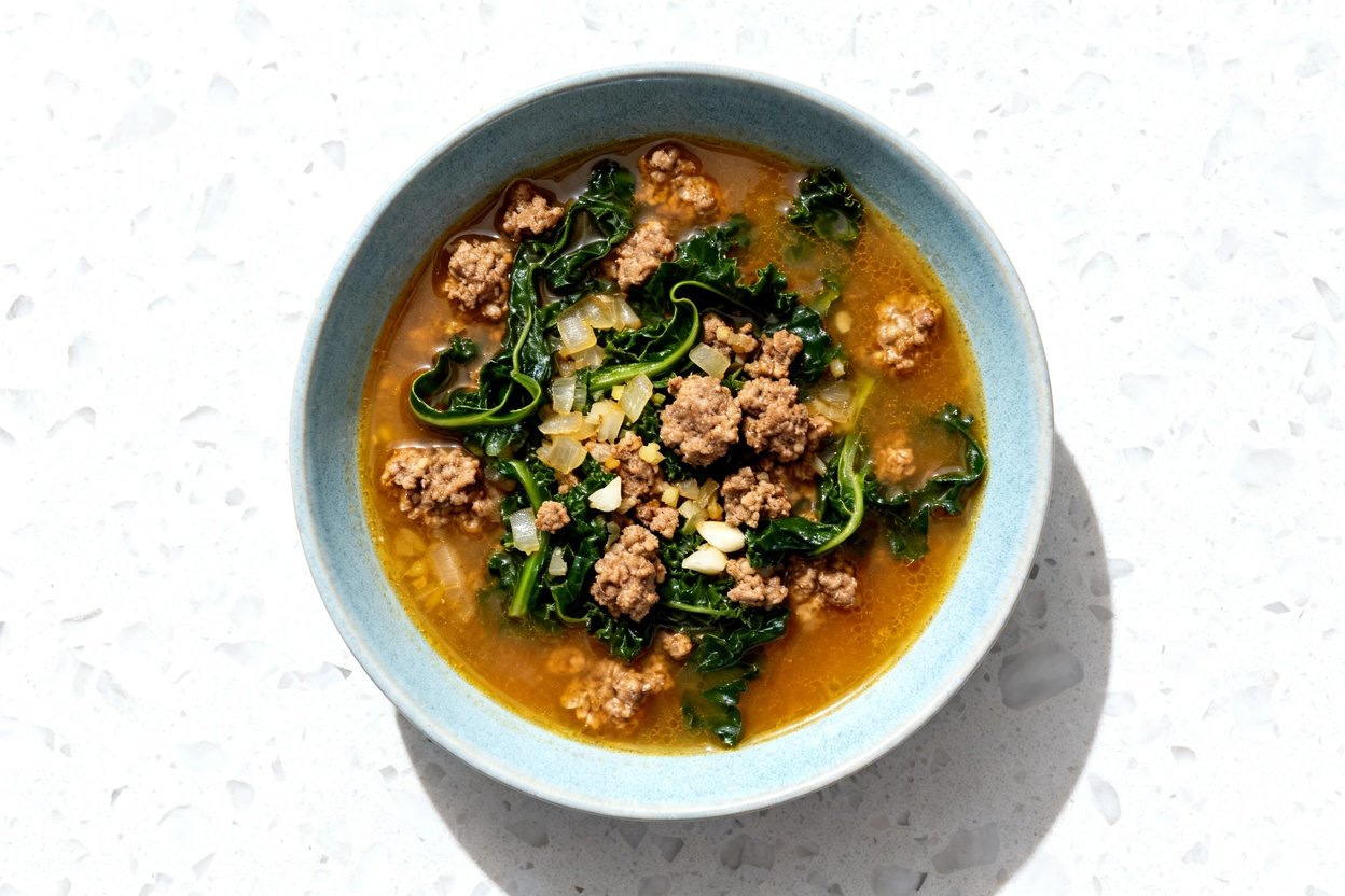 top-down food photo of a single serving bowl of low carb Italian sausage and kale soup, centered and